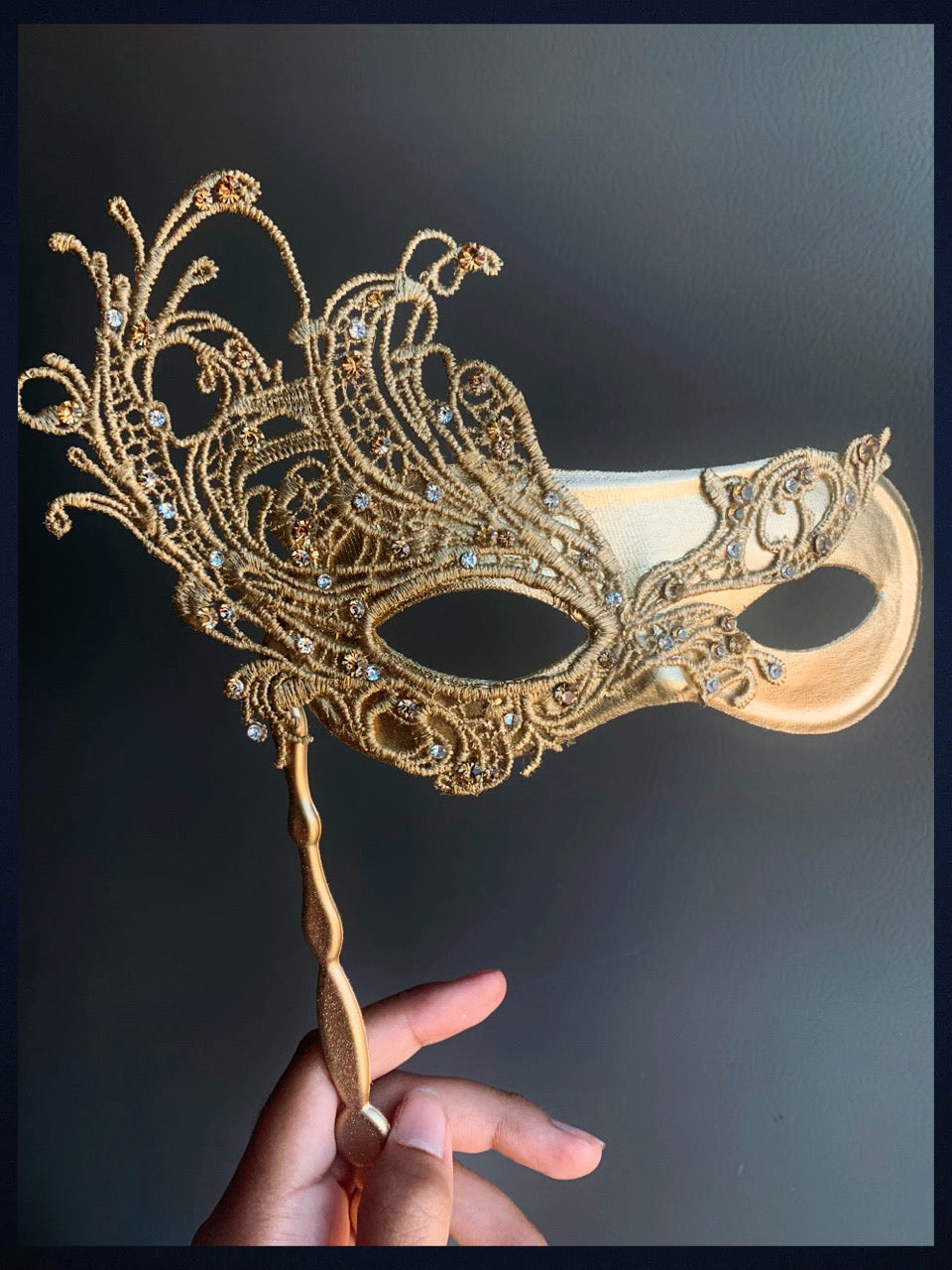 Gold lace handheld masquerade mask with intricate details and rhinestones, part of the Crystal Elegance collection