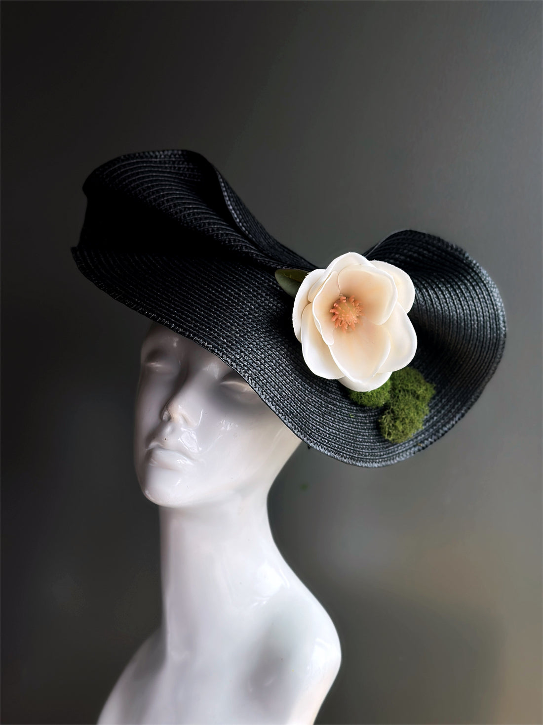 Black fascinator hat with a magnolia and moss.