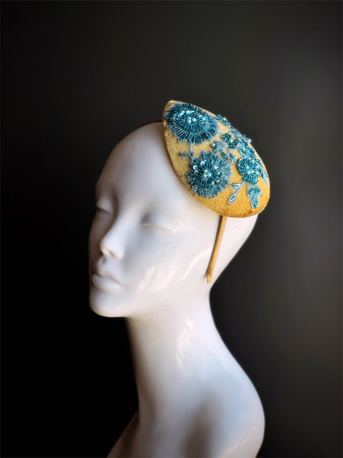 Velvet tear drop shaped fascinator in gold with blue beaded lace design.