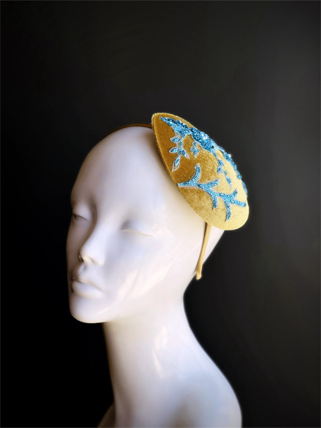Velvet teardrop shaped fascinator in gold with blue beaded lace design.