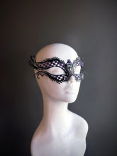 Black metal mask with intricate cutouts and purple rhinestone accents, offering a mysterious and sophisticated design.