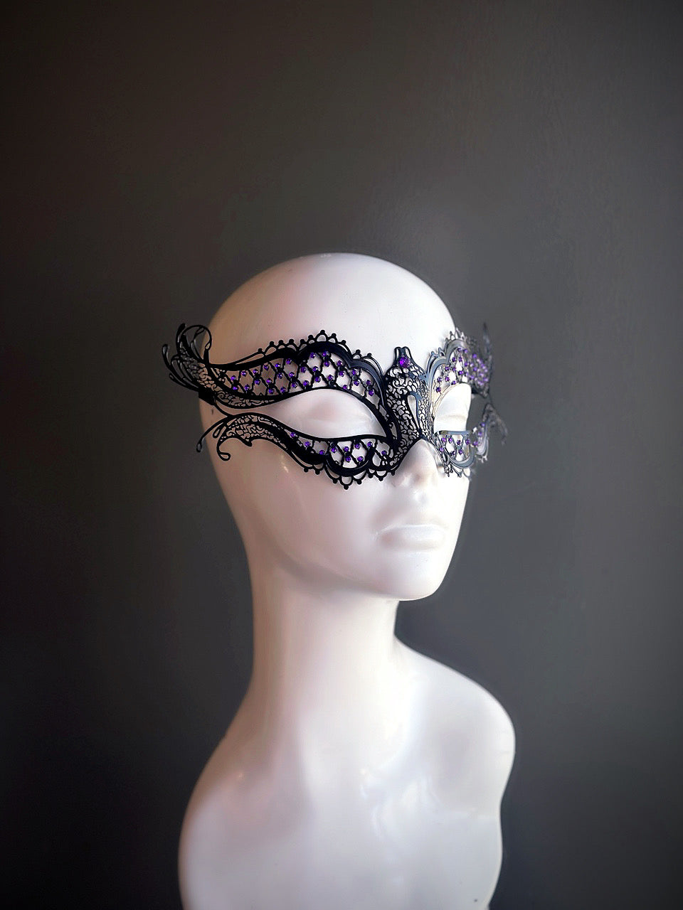 Black metal mask with intricate cutouts and purple rhinestone accents, offering a mysterious and sophisticated design.