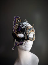 Black and gold masquerade mask with a purple butterfly accent and rhinestone details displayed on a mannequin head.

