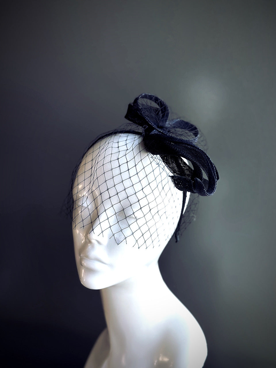 Black fascinator with a net veil and bow accent displayed on a mannequin head.

