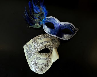 Blue and silver Venetian-style couple masks, one with musical notes and ornate detailing, the other accented with a vibrant blue feather.