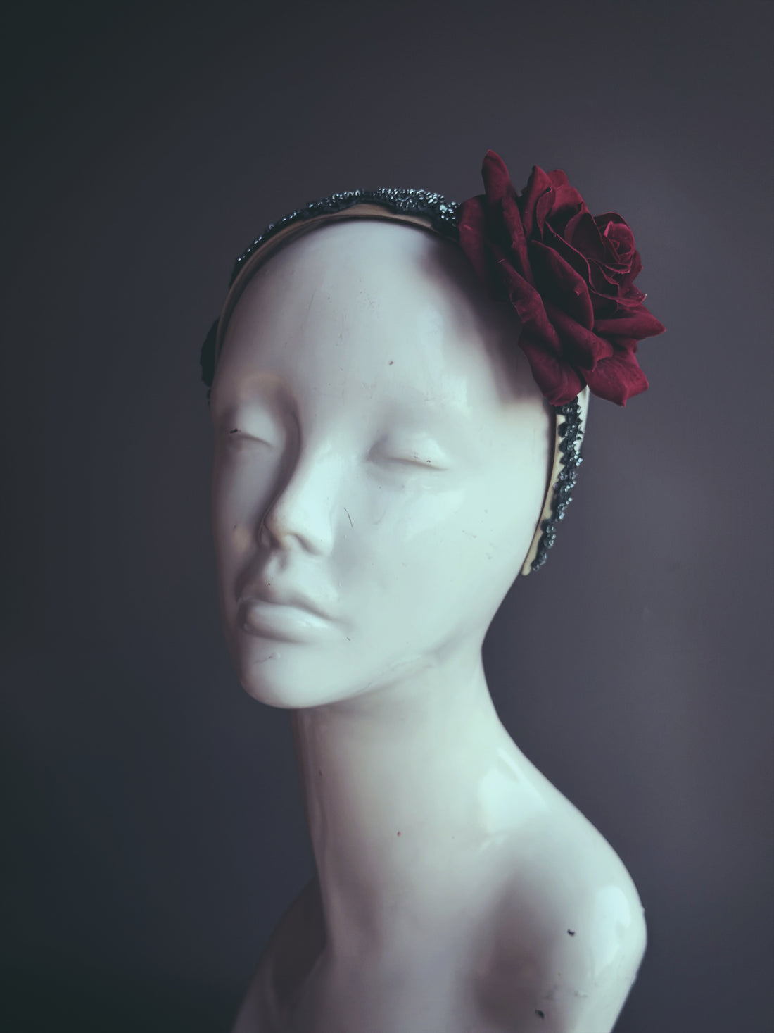 A headband featuring a single burgundy rose with delicate embellishments, styled for formal occasions.