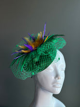 Vibrant Mardi Gras fascinator featuring green netting, purple and gold feathers, and a festive, glowing design.