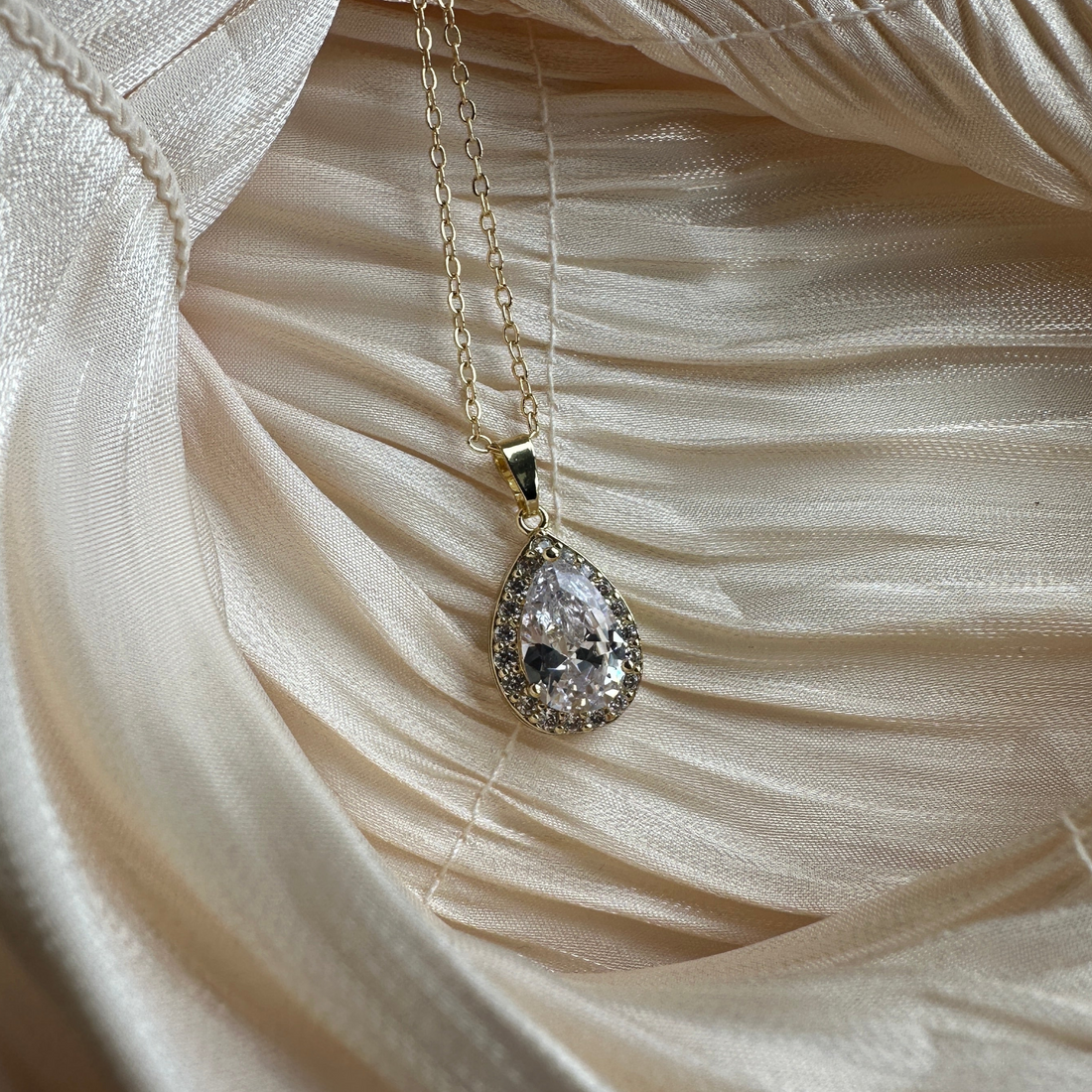  Gold necklace with a teardrop-cut crystal encased in a shimmering halo.