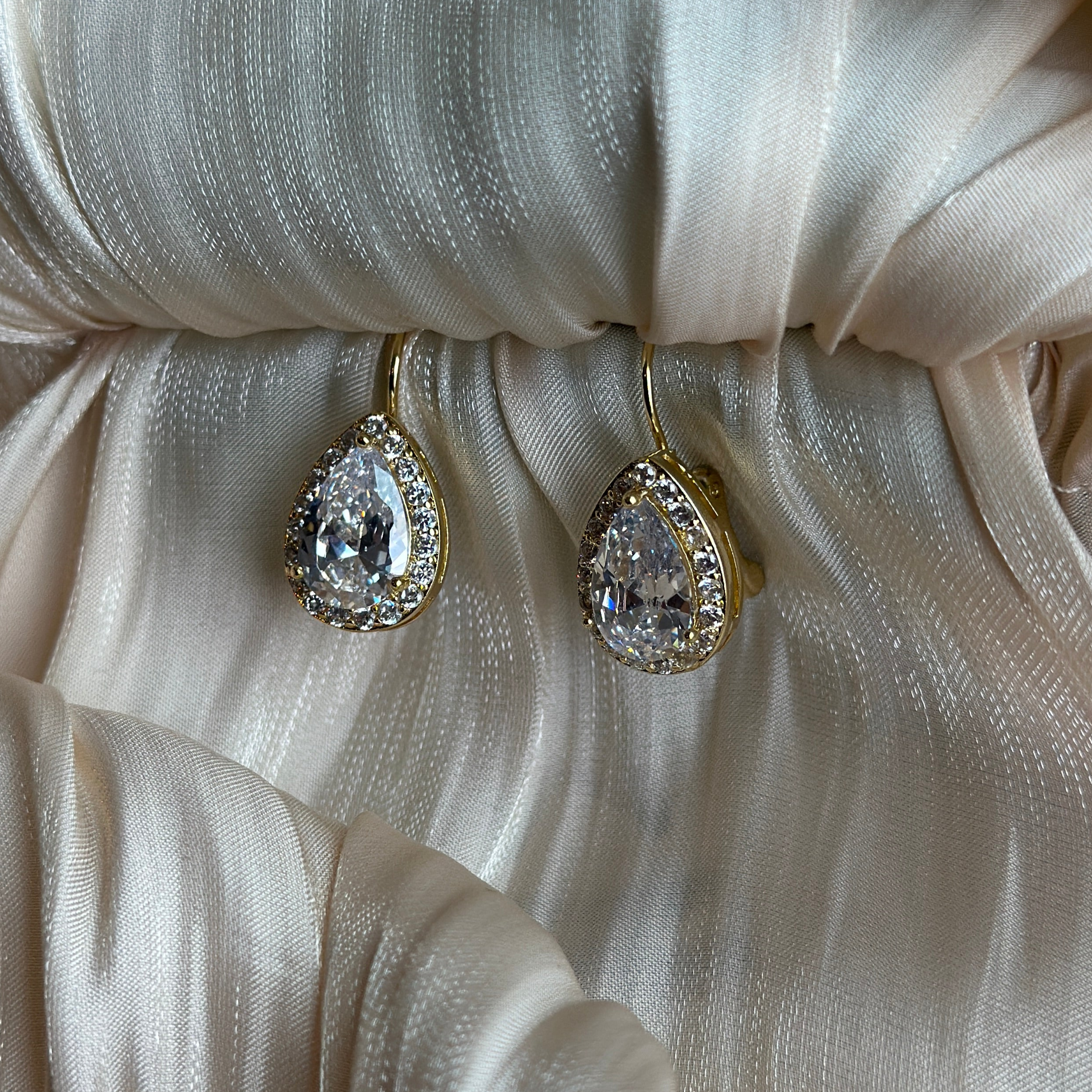 Gold earrings with teardrop-cut crystals framed by a shimmering halo in an elegant drop design.