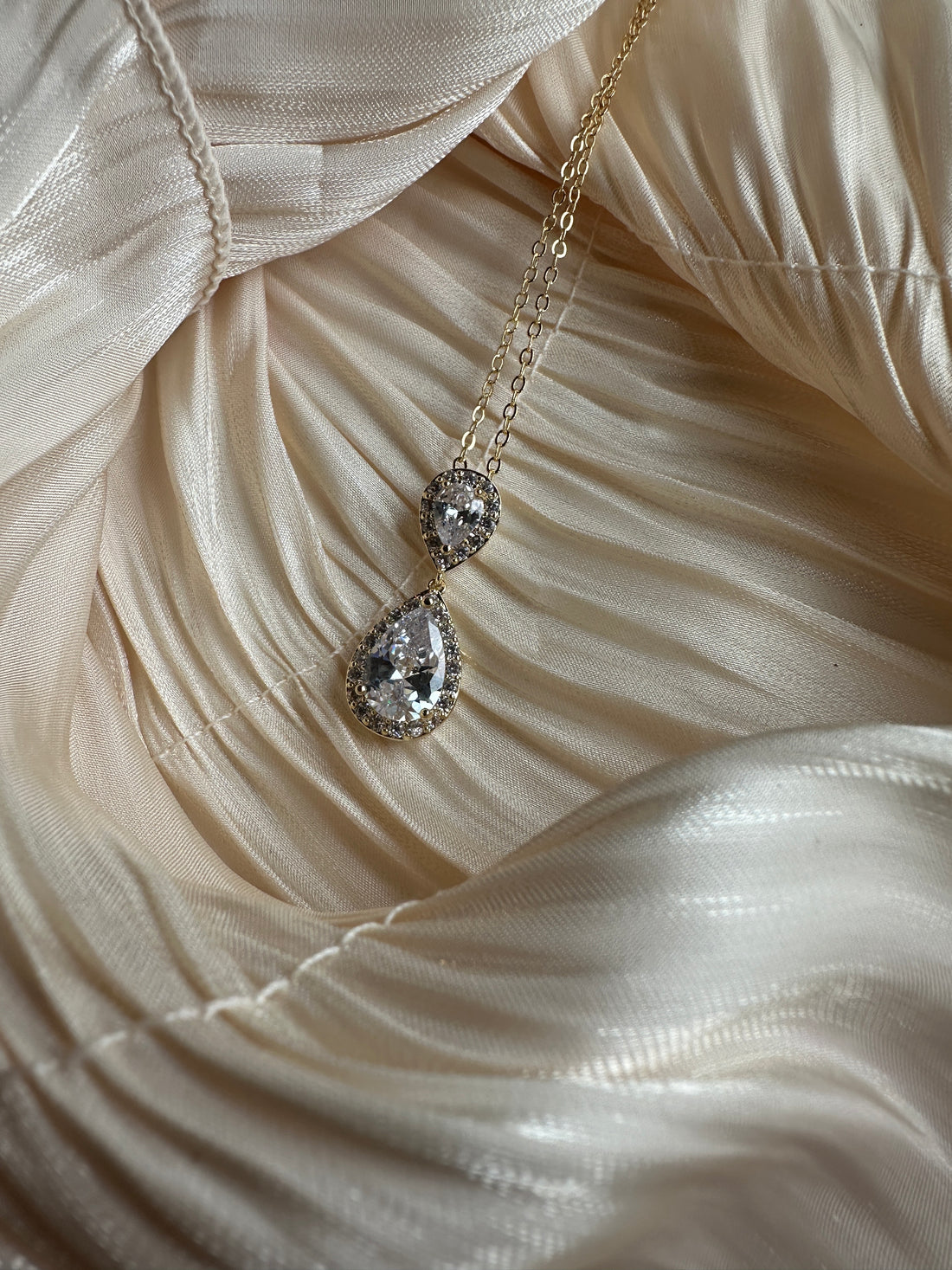 Gold necklace with two teardrop-cut crystals encased in a shimmering halo.