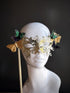 Gold handheld masquerade mask with intricate filigree and butterfly accents displayed on a mannequin head.

