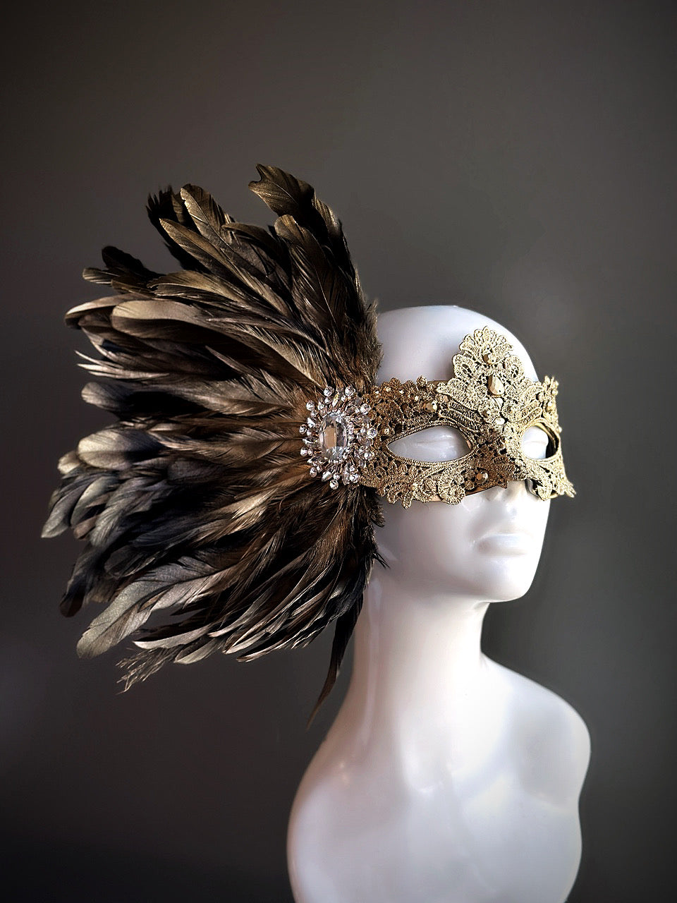 Gold masquerade mask with intricate lace detailing and a dramatic black and gold feather arrangement, perfect for masquerade balls and Venetian parties.

