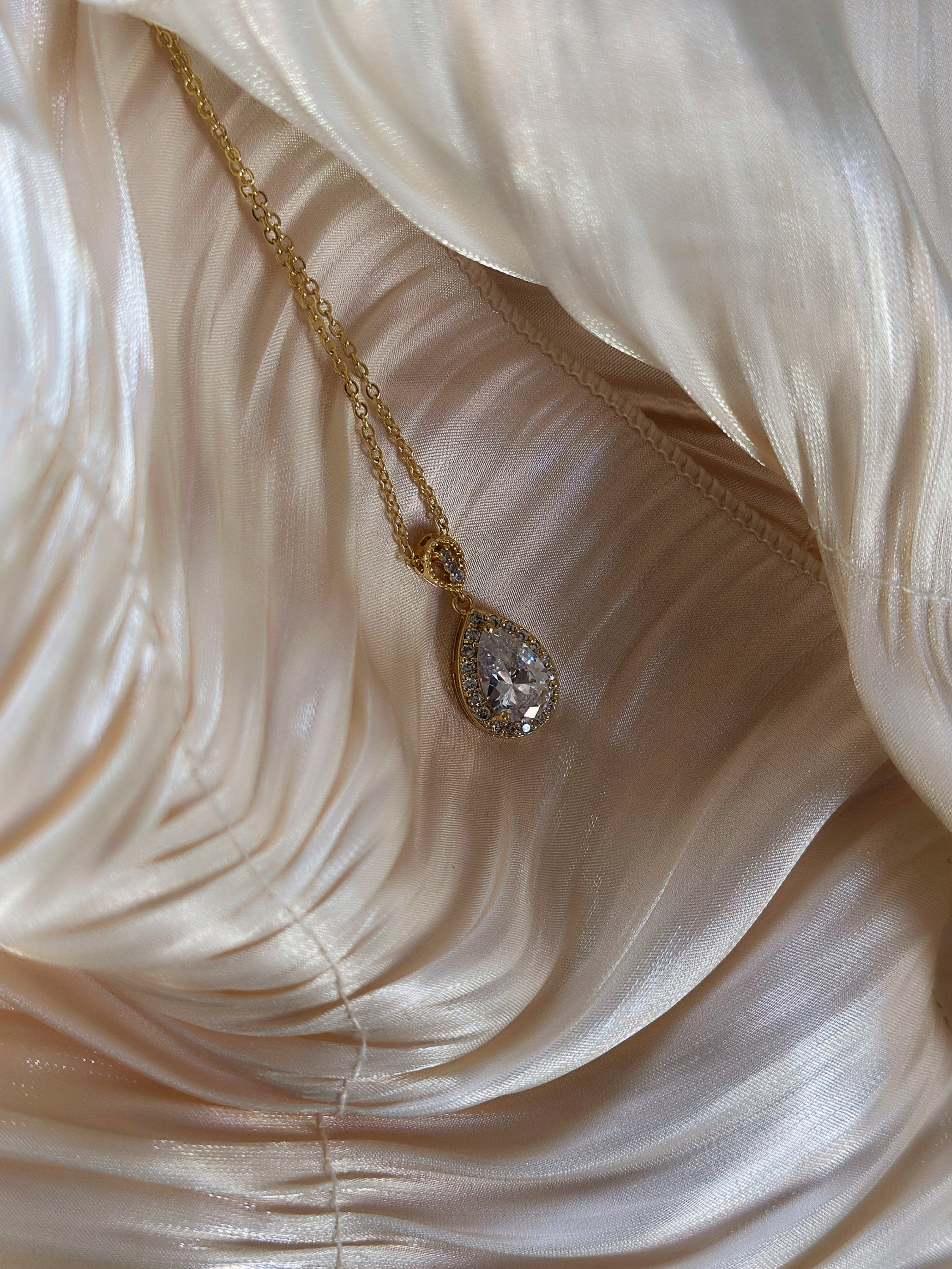 Gold necklace with a teardrop crystal pendant, surrounded by a halo of smaller stones.