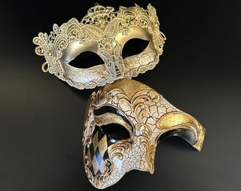 Gold lace Venetian-style mask paired with an ivory mask featuring gold harlequin accents, ideal for formal events and masquerade celebrations.