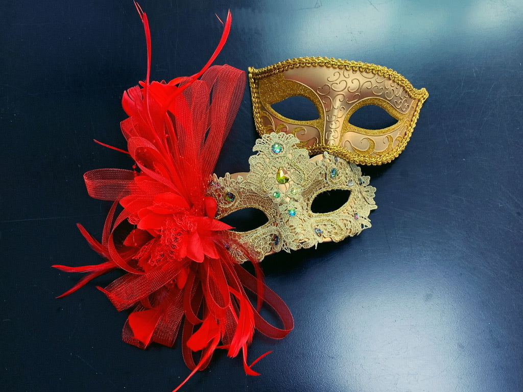 A set of gold masks, one adorned with vibrant red feathers and intricate lace detailing.