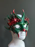 Green and red mask with festive forest-inspired details, including foliage and berries, ideal for holiday-themed events and parties.