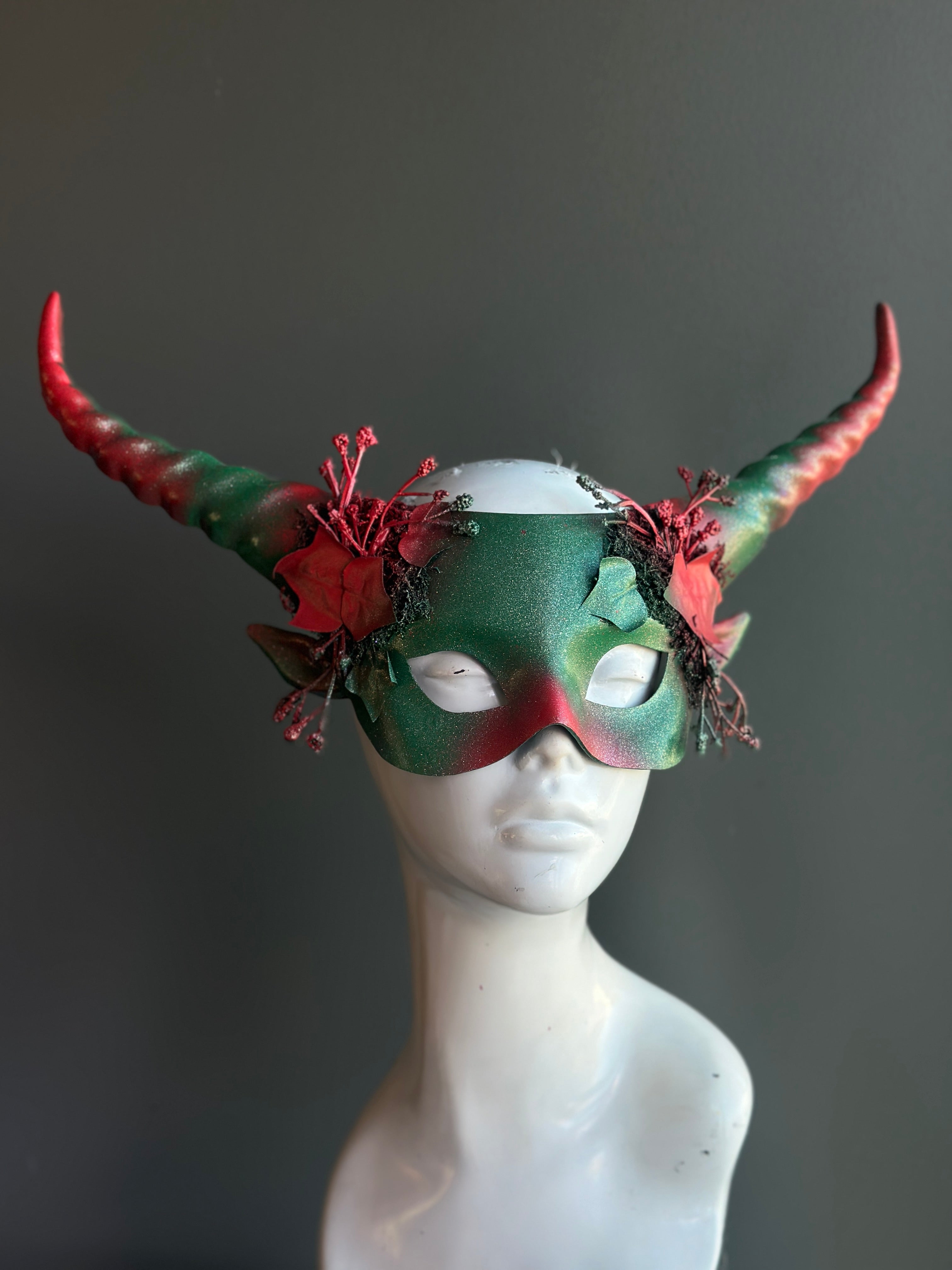 Green and red horned mask with festive foliage and intricate details, ideal for holiday celebrations and themed events.