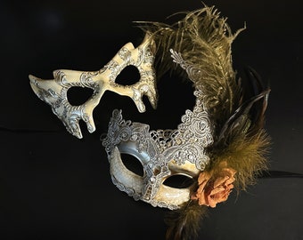 Ivory Venetian-style mask paired with a lace-detailed mask featuring gold feathers and a rose accent, ideal for formal occasions and masquerade events