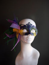 Mardi Gras mask in purple, gold, and green with bold feathers, tulle accents, and intricate sparkling details for a lively and elegant look.