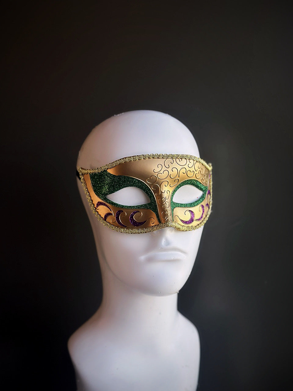 Mardi Gras mask featuring gold, green, and purple tones with intricate swirling patterns and shimmering accents for a festive design.

