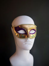 Elegant Mardi Gras mask featuring gold, purple, and green tones with intricate swirling patterns and glitter accents for a sophisticated look.