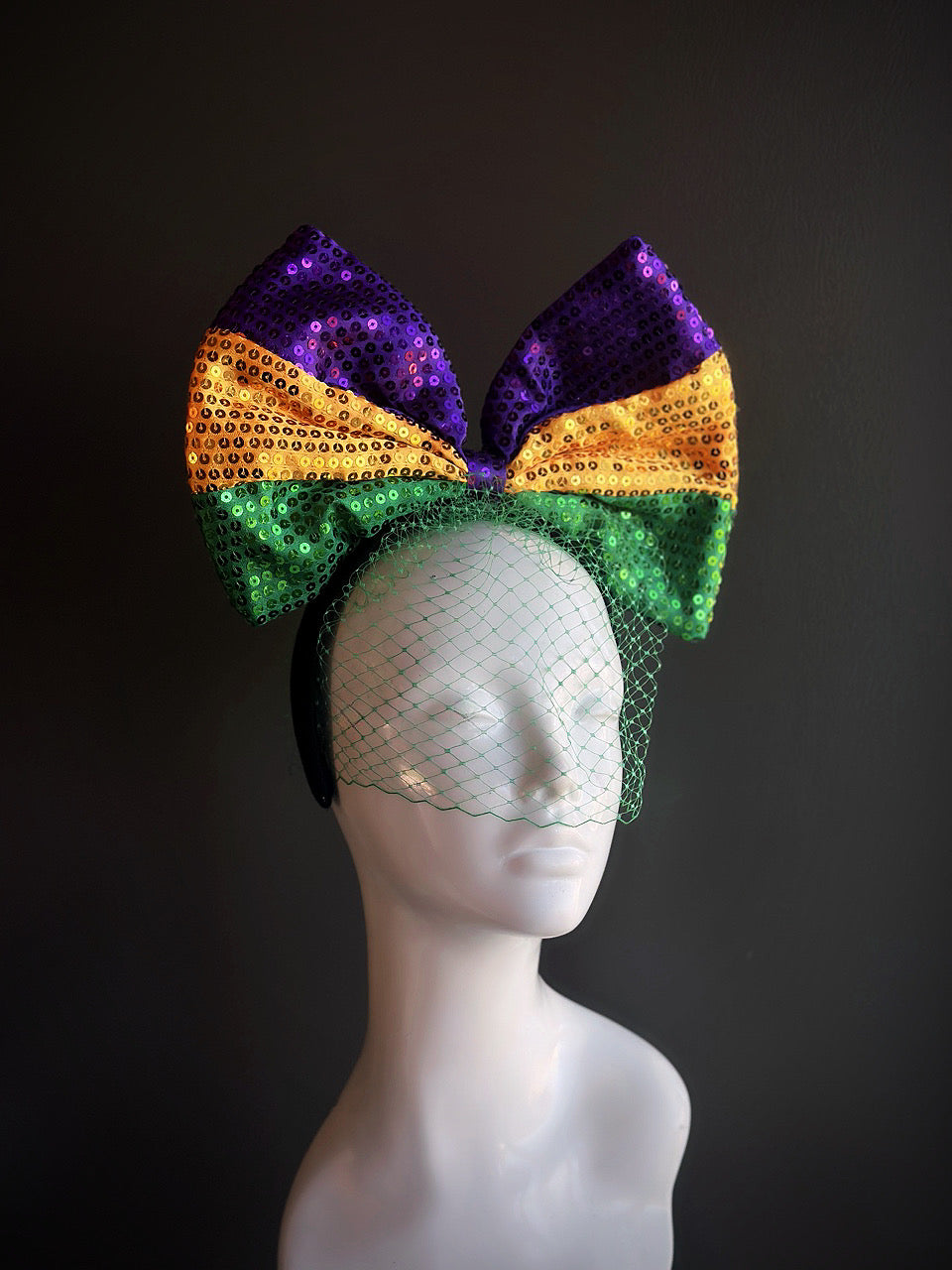 Mardi Gras headpiece featuring a large sequined bow in purple, gold, and green, accented with green netting for a vibrant, festive look.