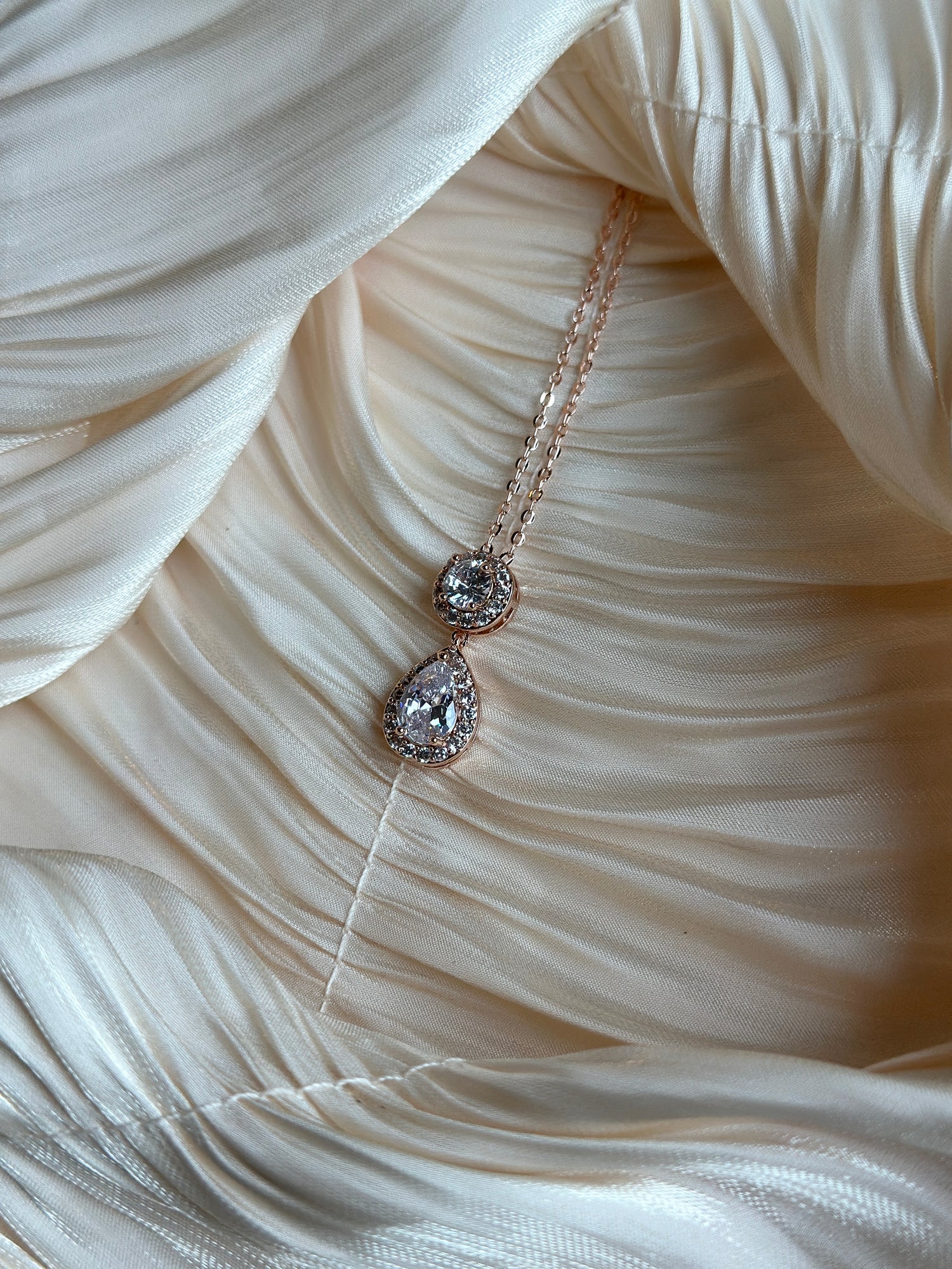 Rose gold necklace with teardrop and round-cut crystals encased in a shimmering halo.