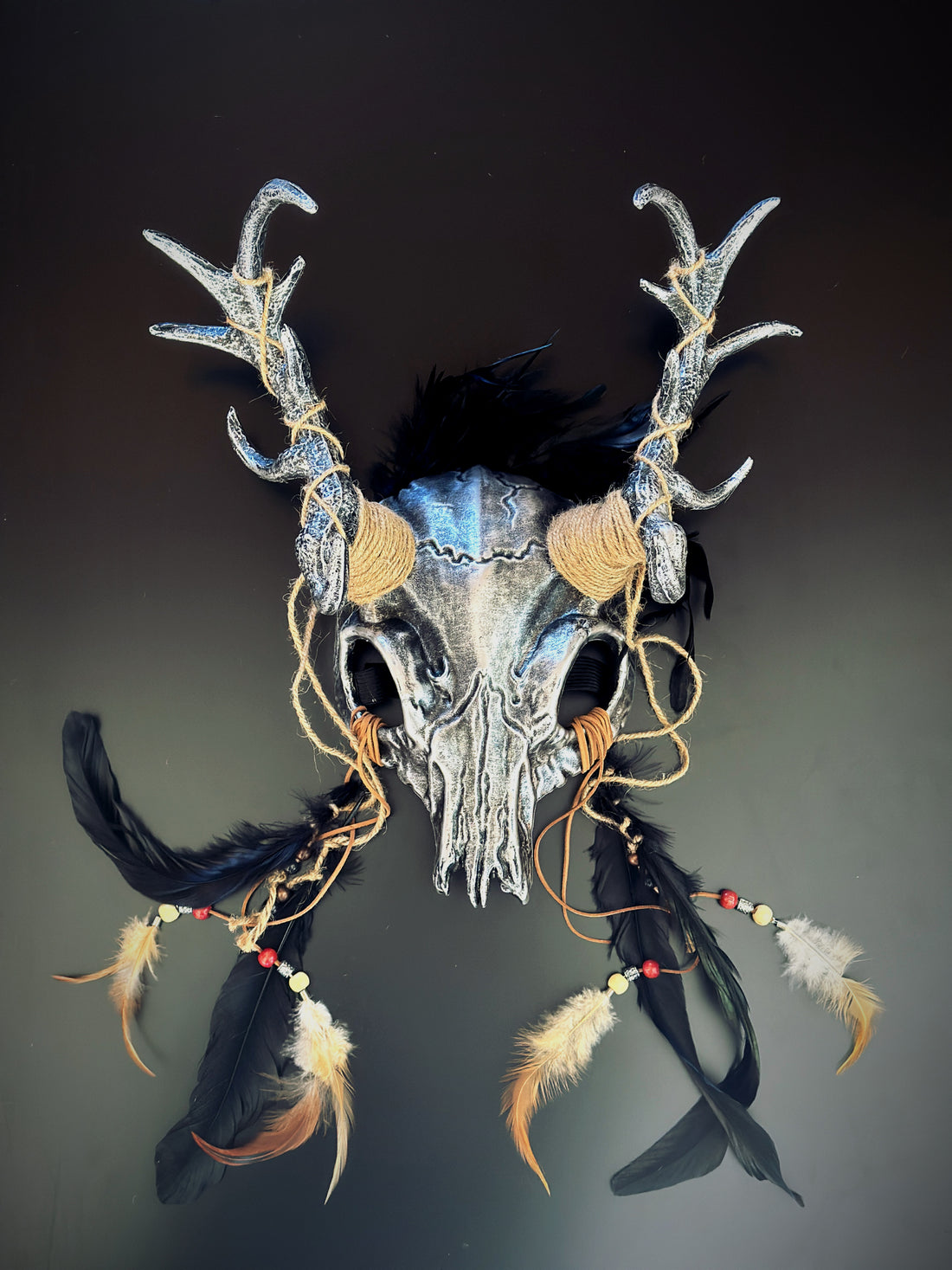 silver-black antler skull headdress with intricate detailing, black feathers, and rustic jute bindings.