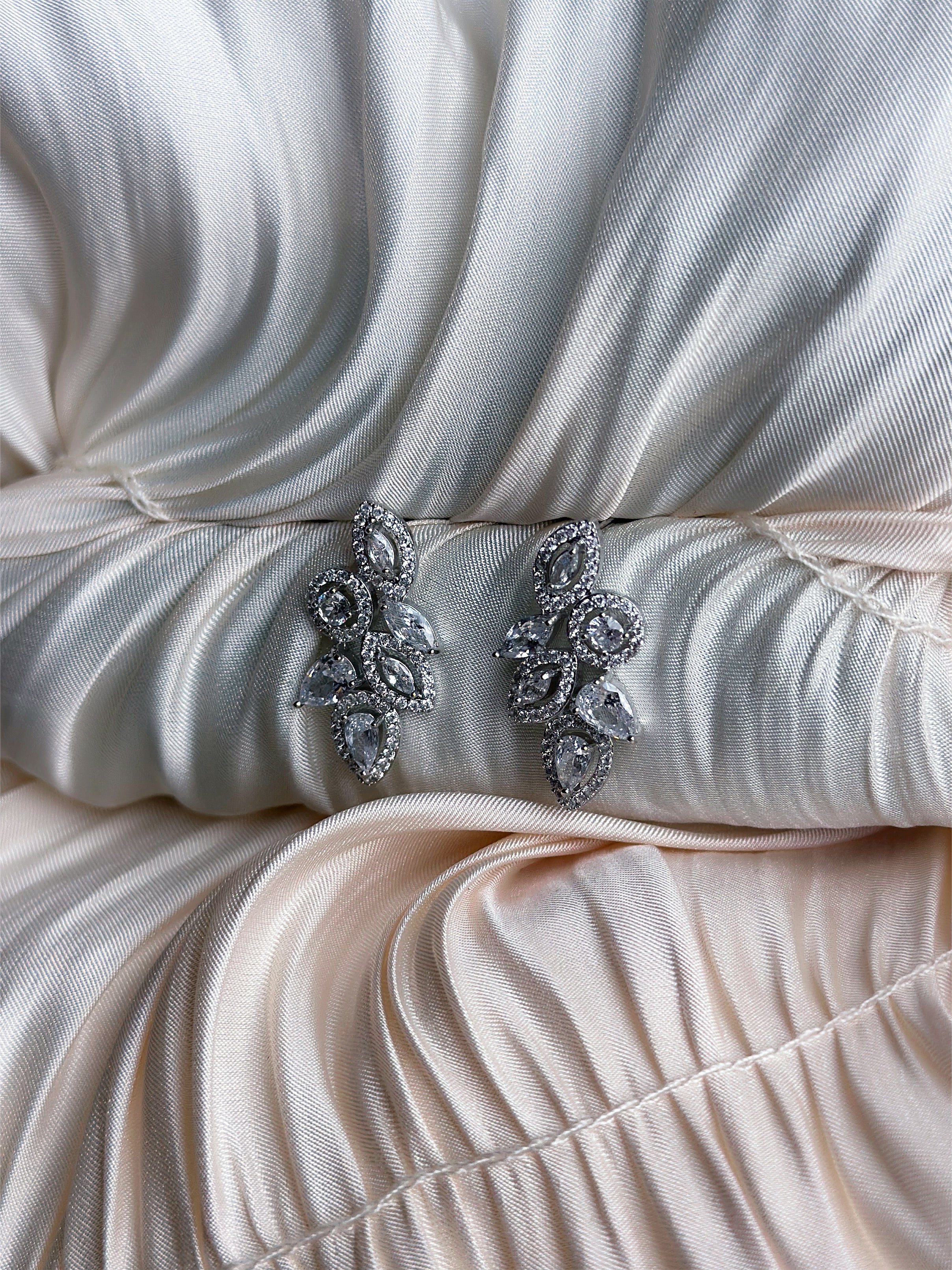 Silver earrings with marquise and teardrop-cut crystals in an elegant leaf-inspired design, displayed on ruched satin fabric.