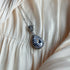 Silver necklace with a teardrop-cut crystal surrounded by a halo of sparkling stones, displayed on ruched satin fabric.