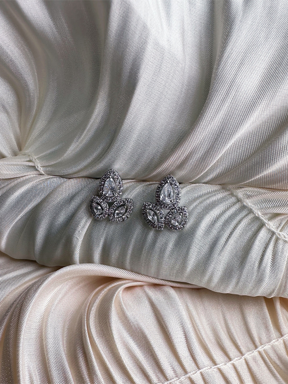 Silver earrings with teardrop and marquise-cut crystals in an intricate floral design, displayed on ruched satin fabric.