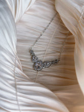 Silver necklace with teardrop and marquise-cut crystals in an elegant butterfly-inspired design, displayed on ruched satin fabric.