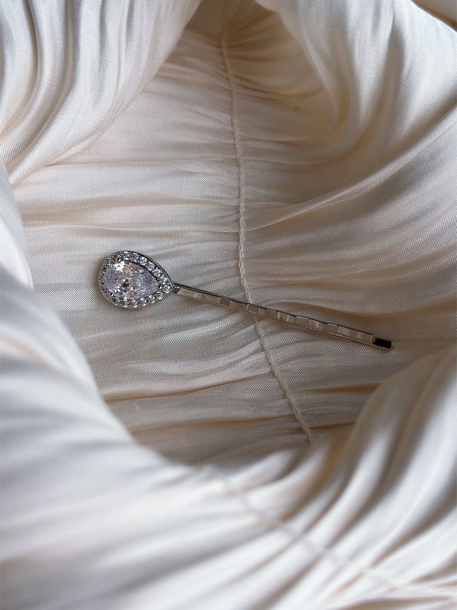 Silver hairpin with a teardrop-cut crystal encircled by a halo of sparkling stones.