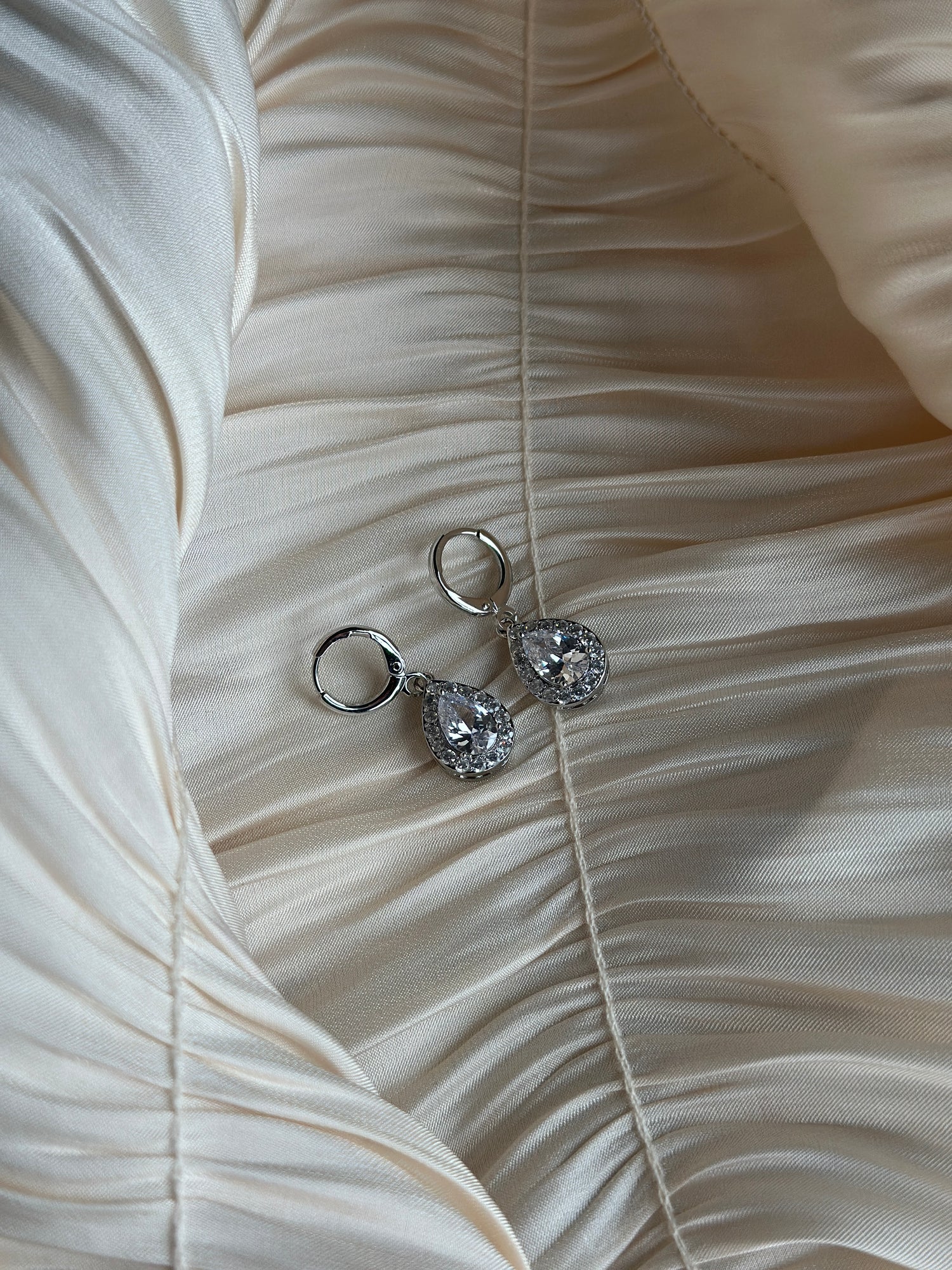 Elegant silver earrings with radiant teardrop crystals on ruched satin fabric.