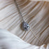 Silver necklace with a teardrop-cut crystal surrounded by a halo of sparkling stones, displayed on ruched satin fabric.