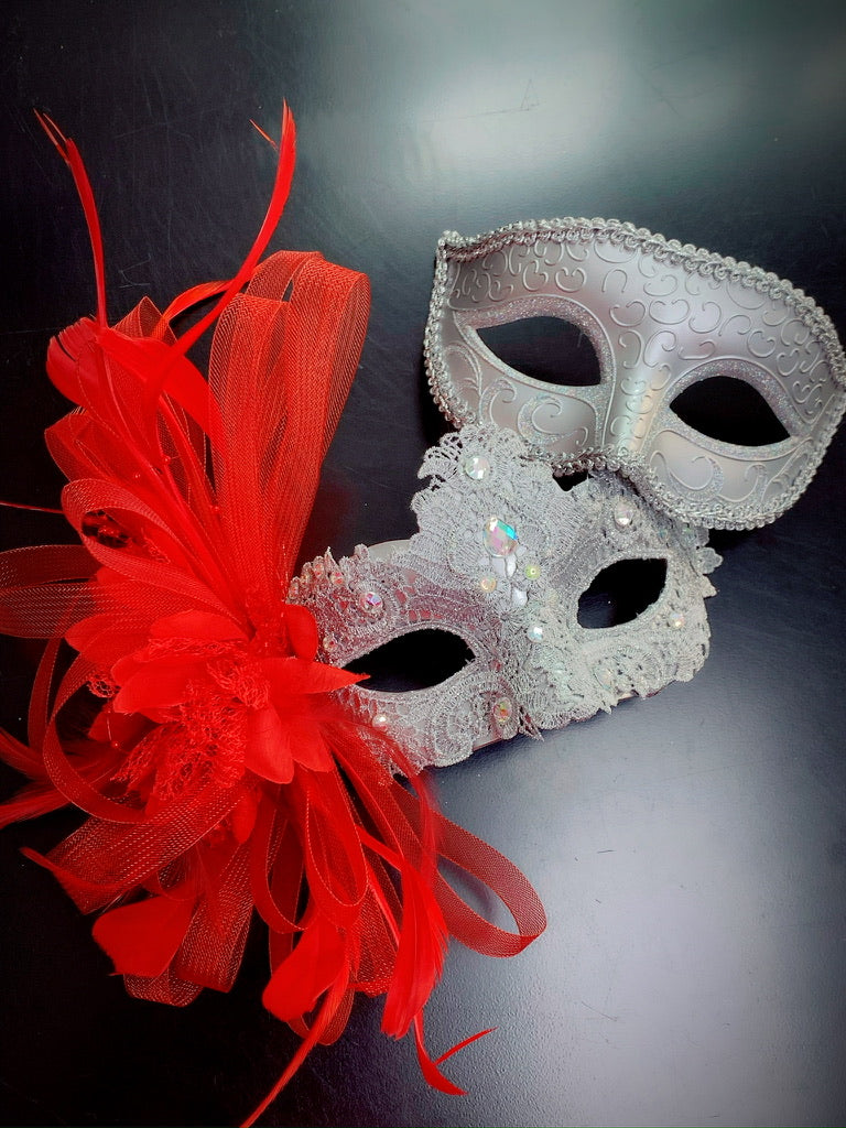 A set of silver masks, one adorned with vibrant red feathers and intricate lace detailing.