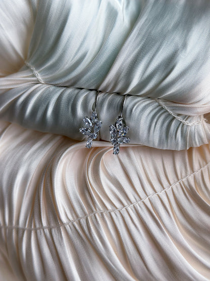 Silver earrings with marquise-cut crystals in a branch design, displayed on ruched satin fabric.