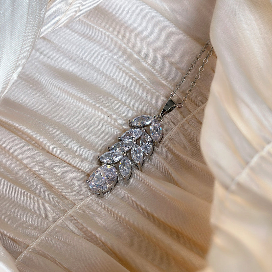 Silver necklace with marquise and teardrop-cut crystals in a cascading leaf design, displayed on ruched satin fabric.