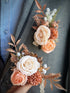 A beautifully crafted artificial floral boutonniere and corsage set featuring roses in shades of rustic peaches and creams