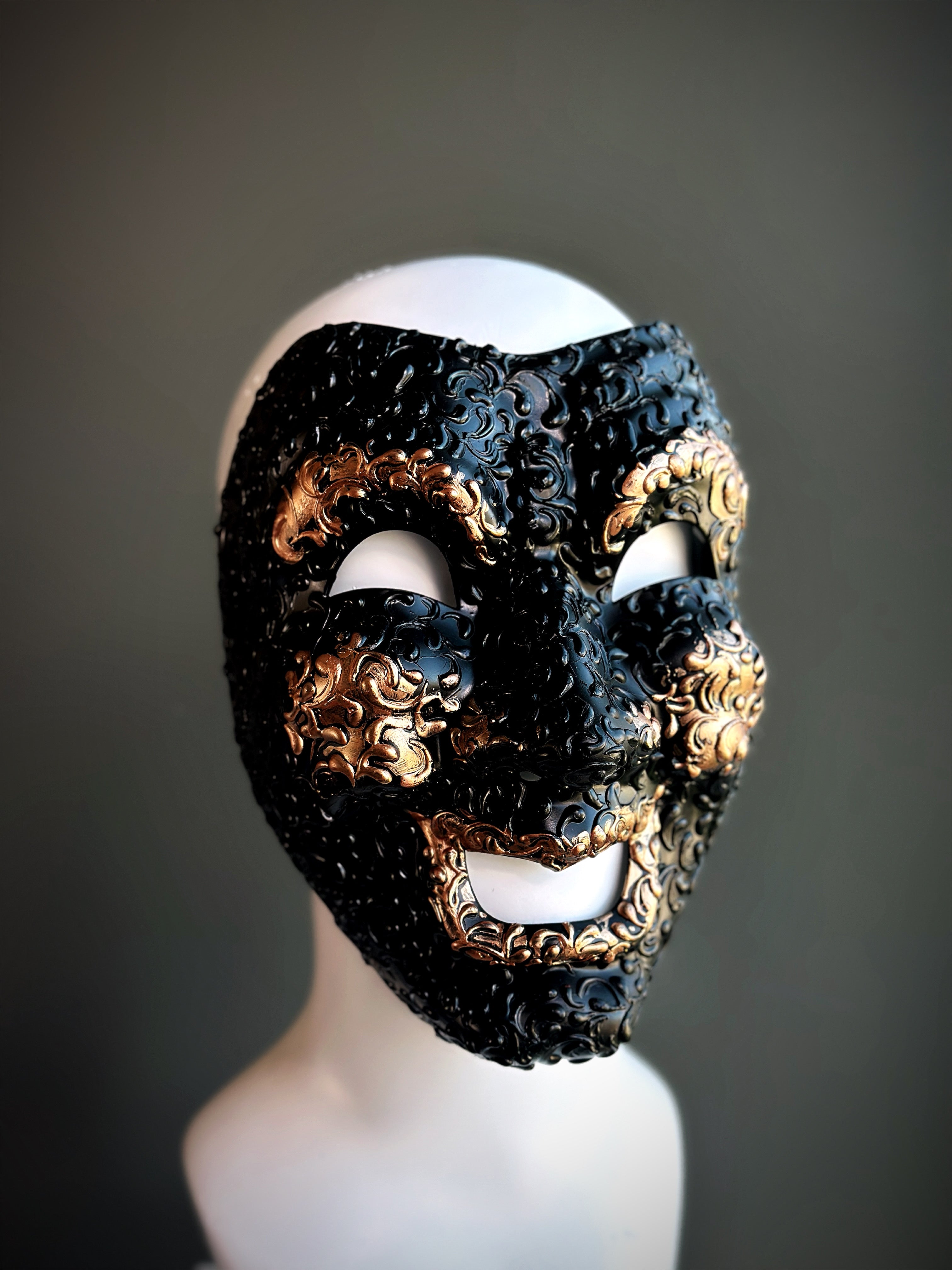 Venetian comedy mask in black with gold detailing, featuring an expressive smiling design and intricate raised accents.

