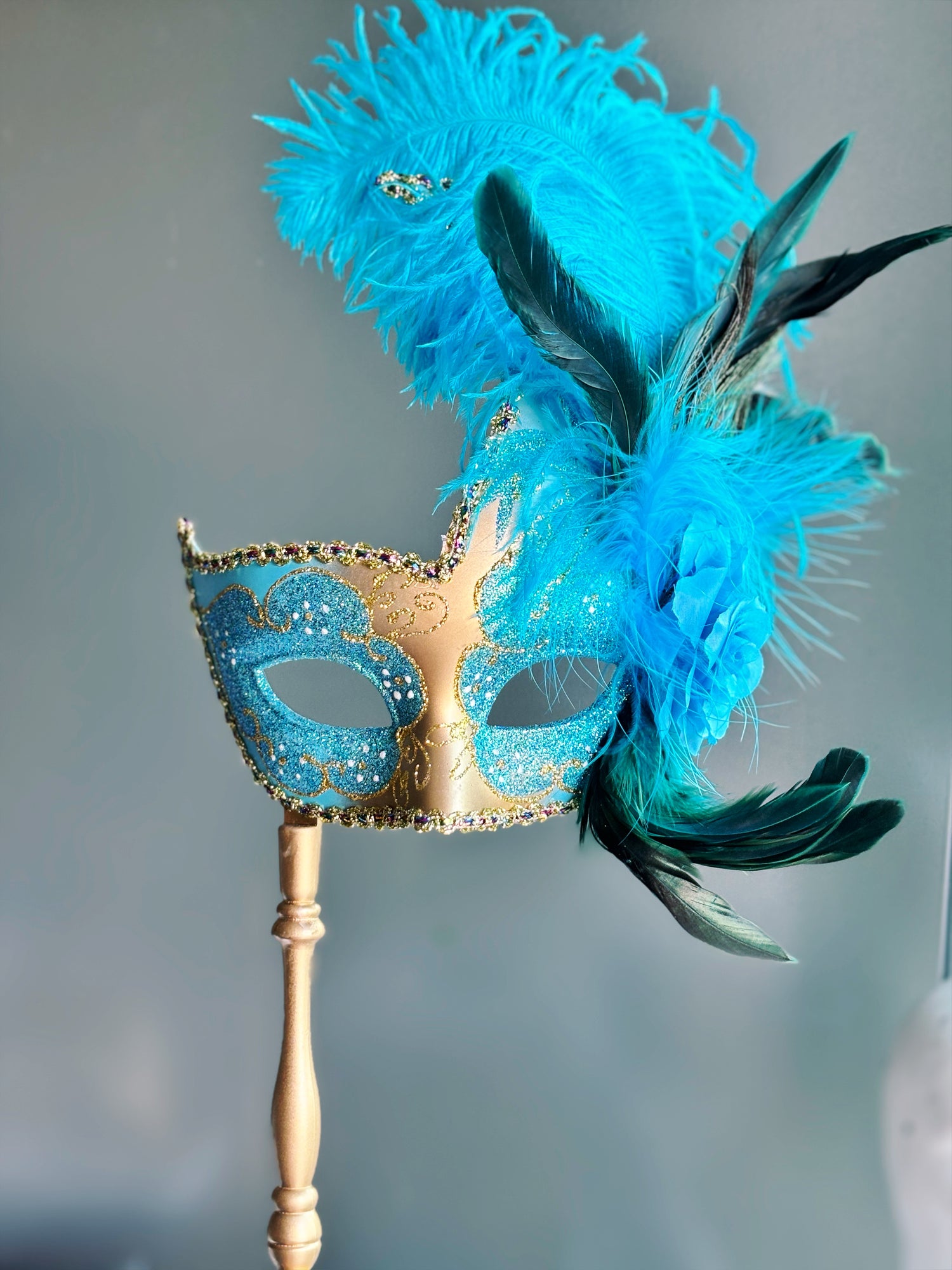 Turquoise and gold Venetian mask for women, adorned with glitter accents and vibrant feathers, perfect for formal events.