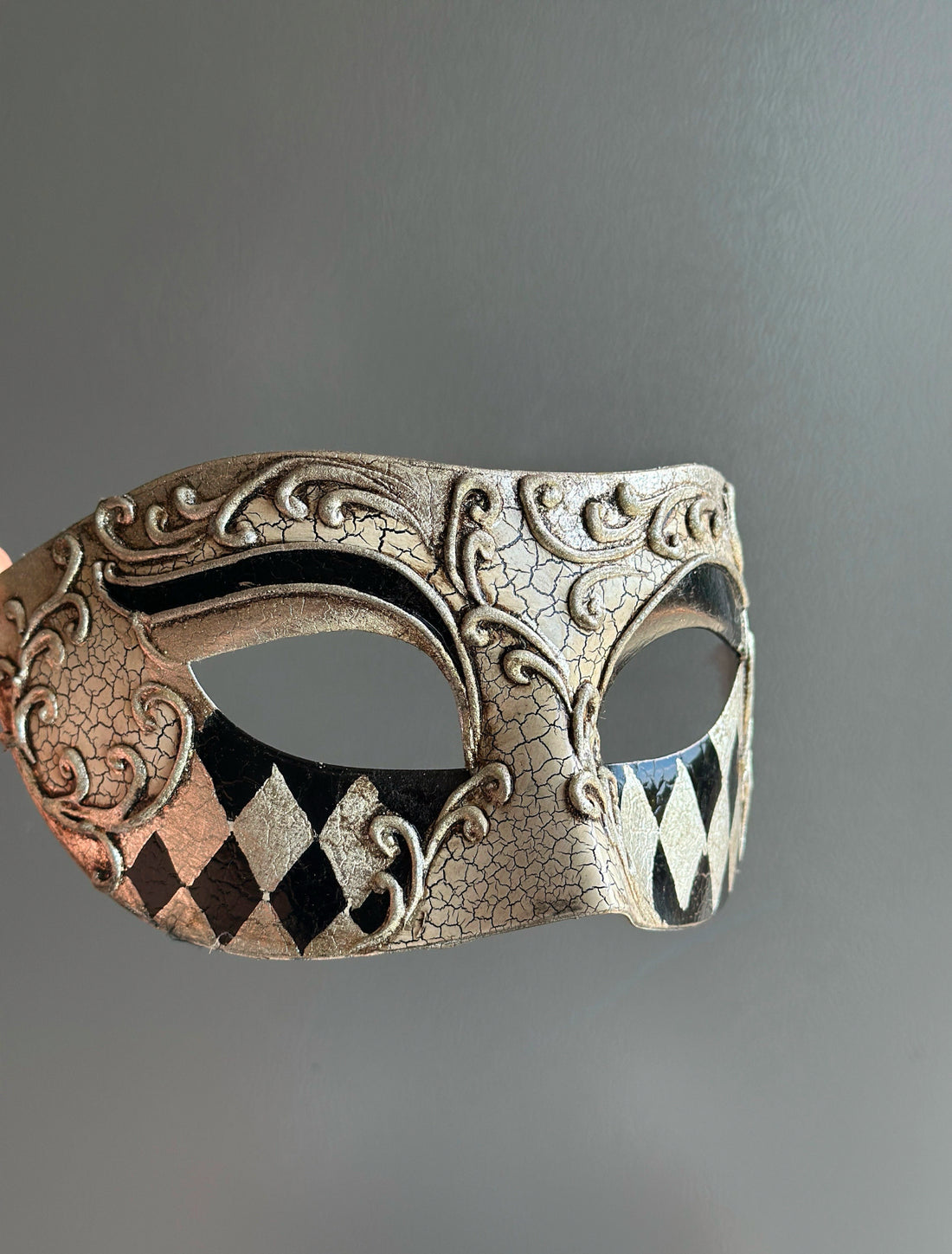 Venetian mask with antique crackle finish, scrollwork detailing, and black and silver harlequin patterns, ideal for masquerades and formal occasions.

